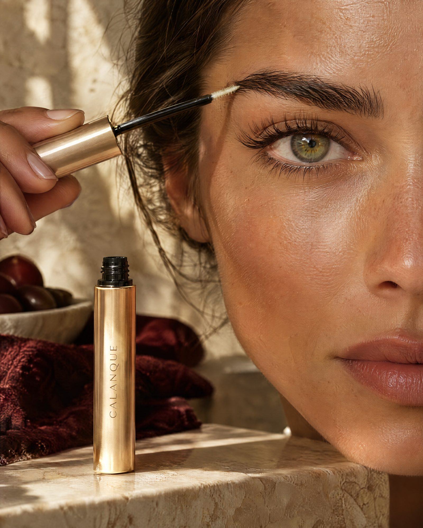 A gold brow wand brushing through a full brow